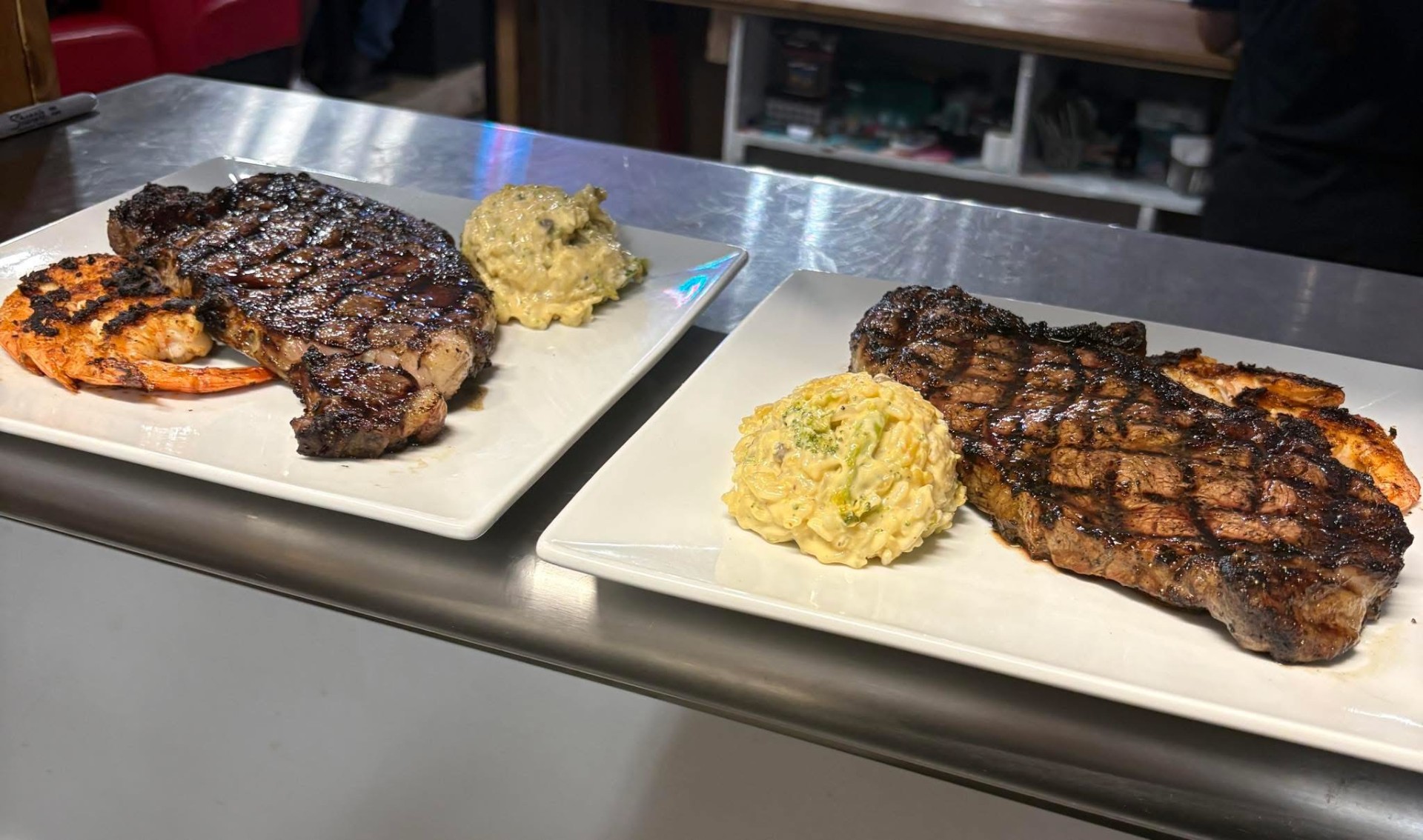 Grilled ribeye steaks with shrimp and broccoli mac on the pass